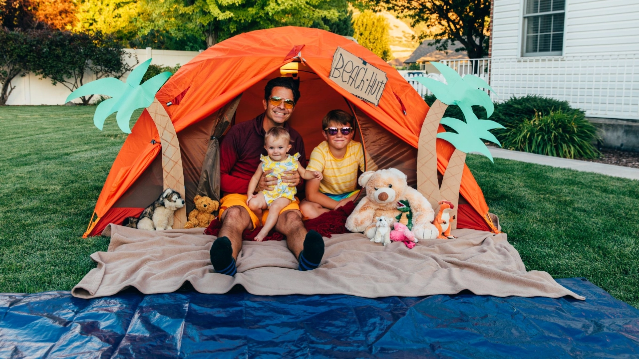 Vater sitzt mit Kindern in Zelthuette im Garten