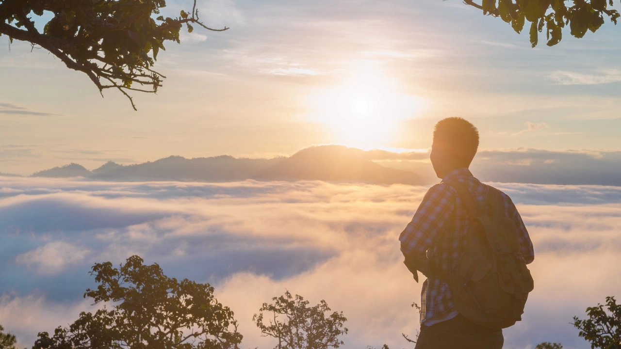 Ein junger Mann genießt auf einem Berggipfel den Sonnenuntergang